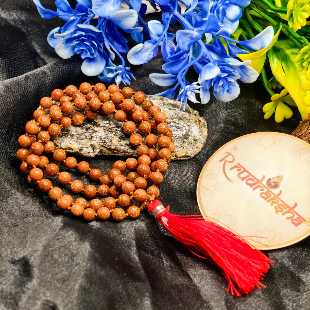 Sun stone beaded necklace with a red tassel on a dark fabric background with flowers.