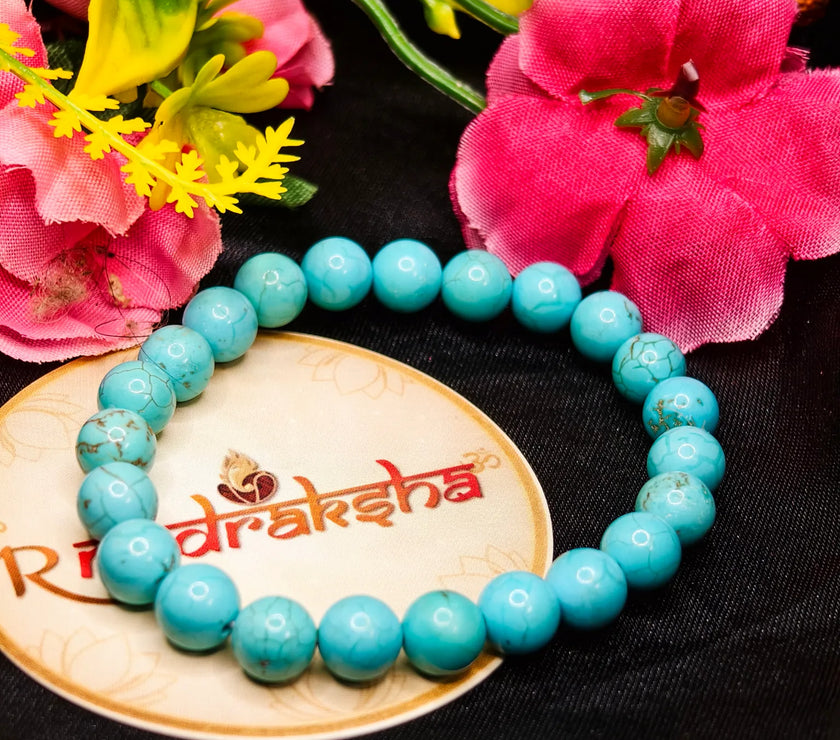 Turquoise beaded bracelet on a wooden plate with flowers in the background. Premium products with lab certificate. Firoza Bracelet 
