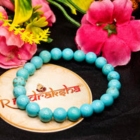 Turquoise beaded bracelet on a wooden plate with flowers in the background. Premium products with lab certificate. Firoza Bracelet 