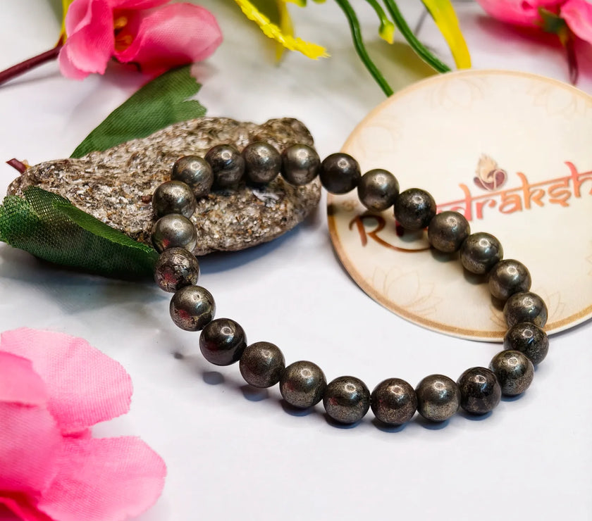 Pyrite bracelet Lab Certified product bracelet on a white surface with pink flowers and a stone. 