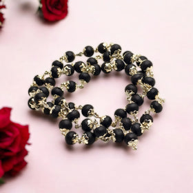 Karungali Ebony Wood beaded necklace made up with German Silver with gold accents on a pink background with red roses.