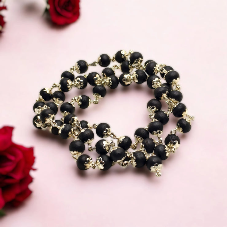 Karungali Ebony Wood beaded necklace made up with German Silver with gold accents on a pink background with red roses.