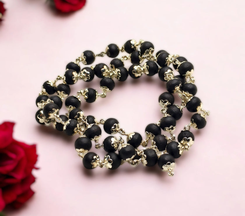 Karungali Ebony Wood beaded necklace made up with German Silver with gold accents on a pink background with red roses.