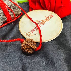 Ganesh Rudraksha bead with red thread on a gold disc with 'Rudraksha' text, on a dark fabric background.