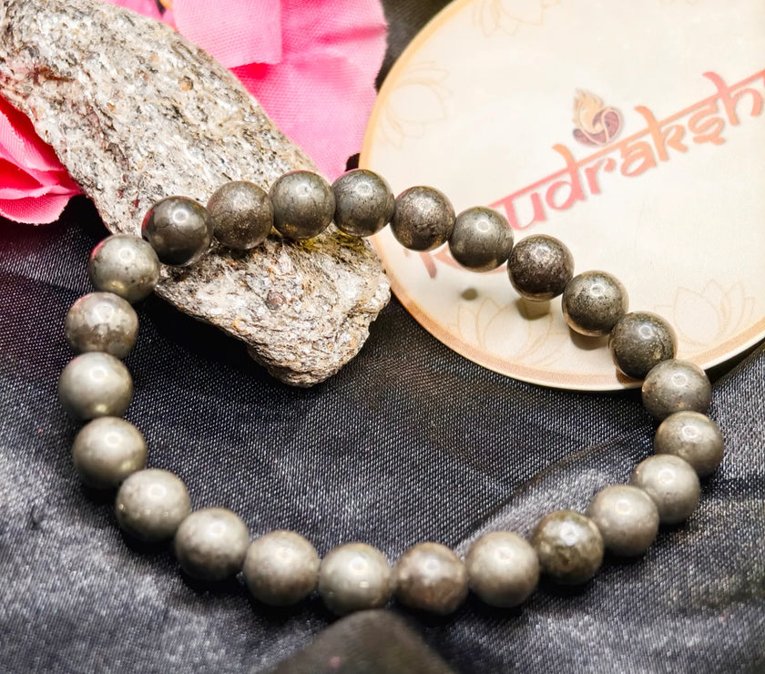 Pyrite Beaded bracelet Lab Certified on a rock with pink flowers and a branded container in the background