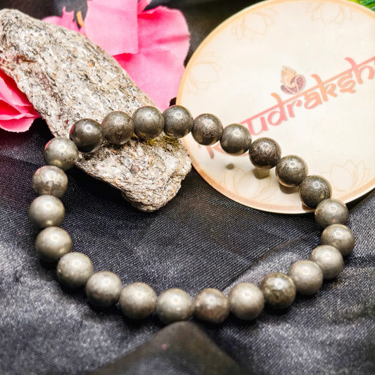 Pyrite Beaded bracelet Lab Certified on a rock with pink flowers and a branded container in the background