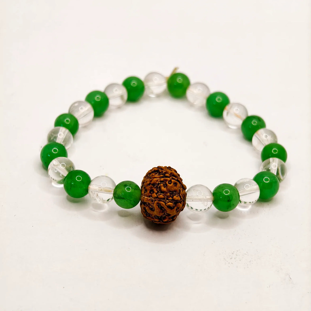 Bracelet with green and clear beads and a brown rudraksha stone on a white background