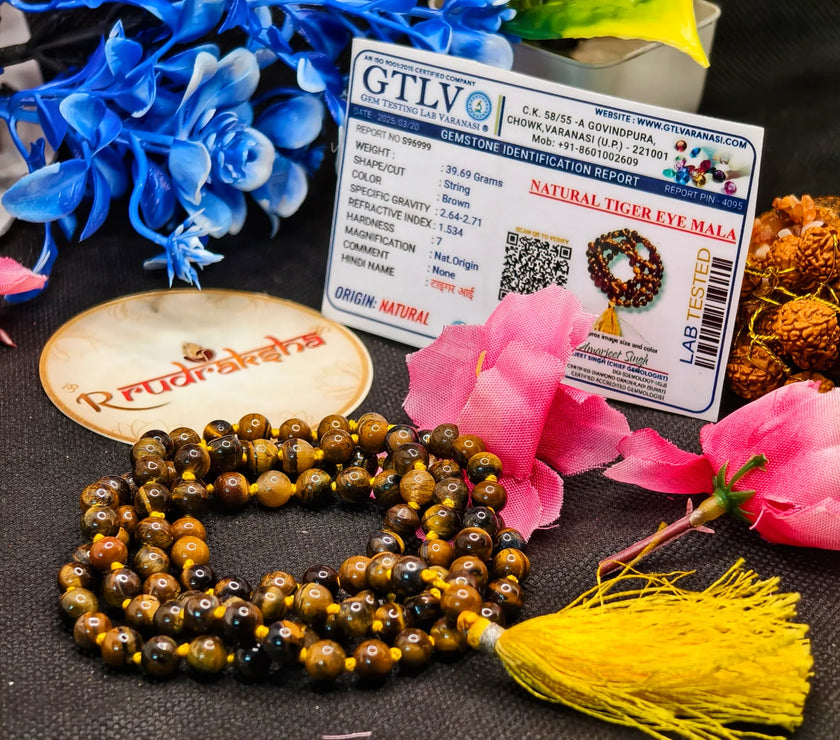 Tiger eye mala with lab identification report and Radhakrishna logo on a textured surface with flowers.